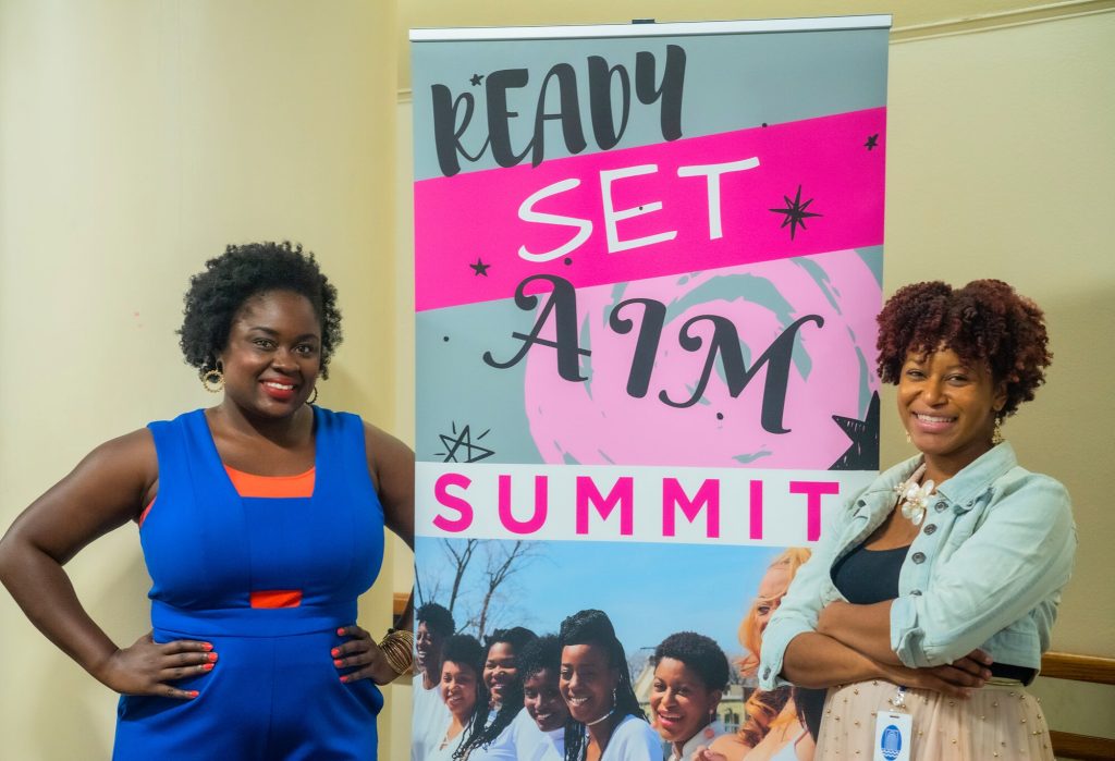 Two black women standing in front of a summit promotion banner